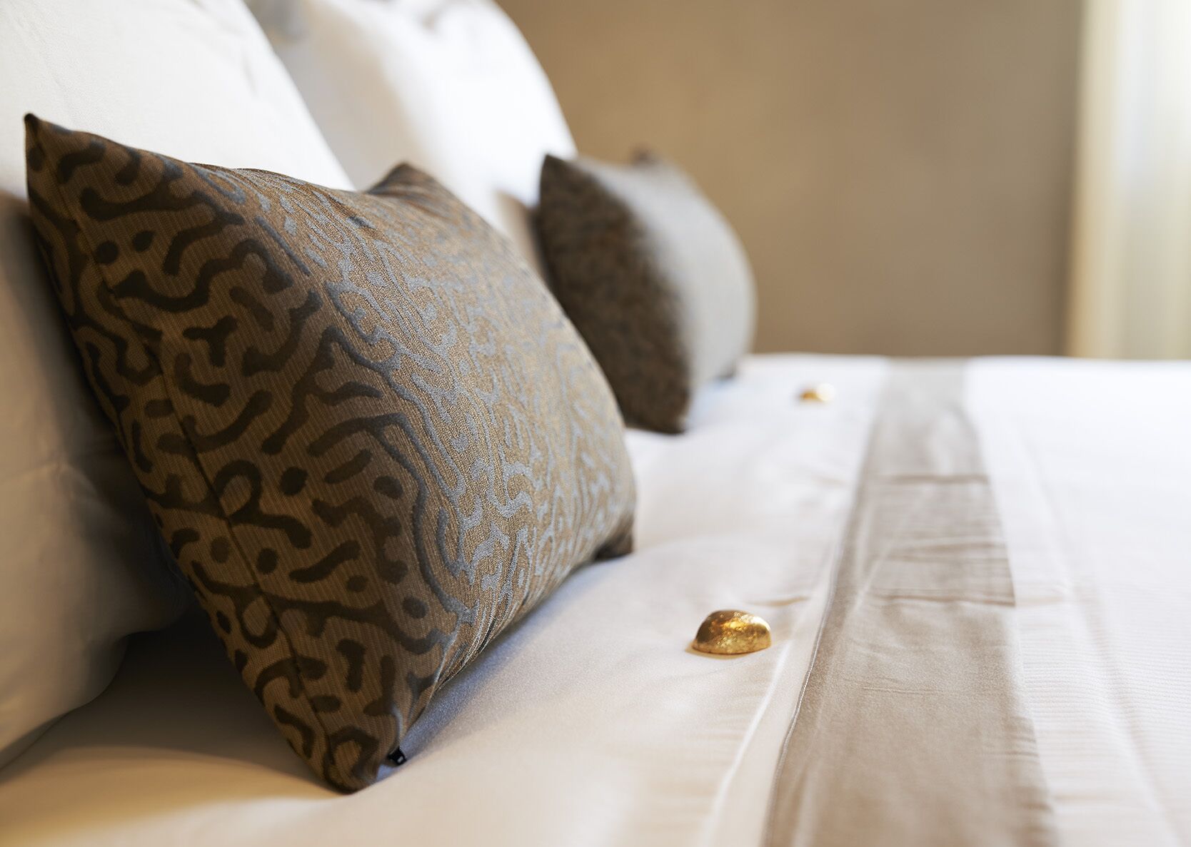 Una cama bien hecha con almohadones estampados y un adorno dorado sobre el edredón.