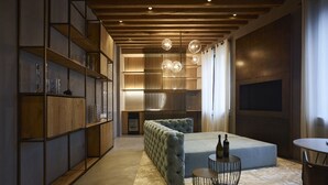 A modern bedroom with a large bed, a seating area with a round table, and built-in shelving. - Fornace Suite (Florence)