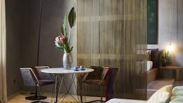 Una habitación moderna con una mesa redonda, dos sillas, un jarrón decorativo con flores y un separador con líneas verticales.