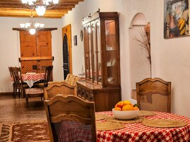 Uma sala de jantar com mesa de madeira, cadeiras, armário e lustre.