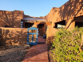 Uma passagem que leva a um edifício com portão azul, cercado por muros e vegetação.