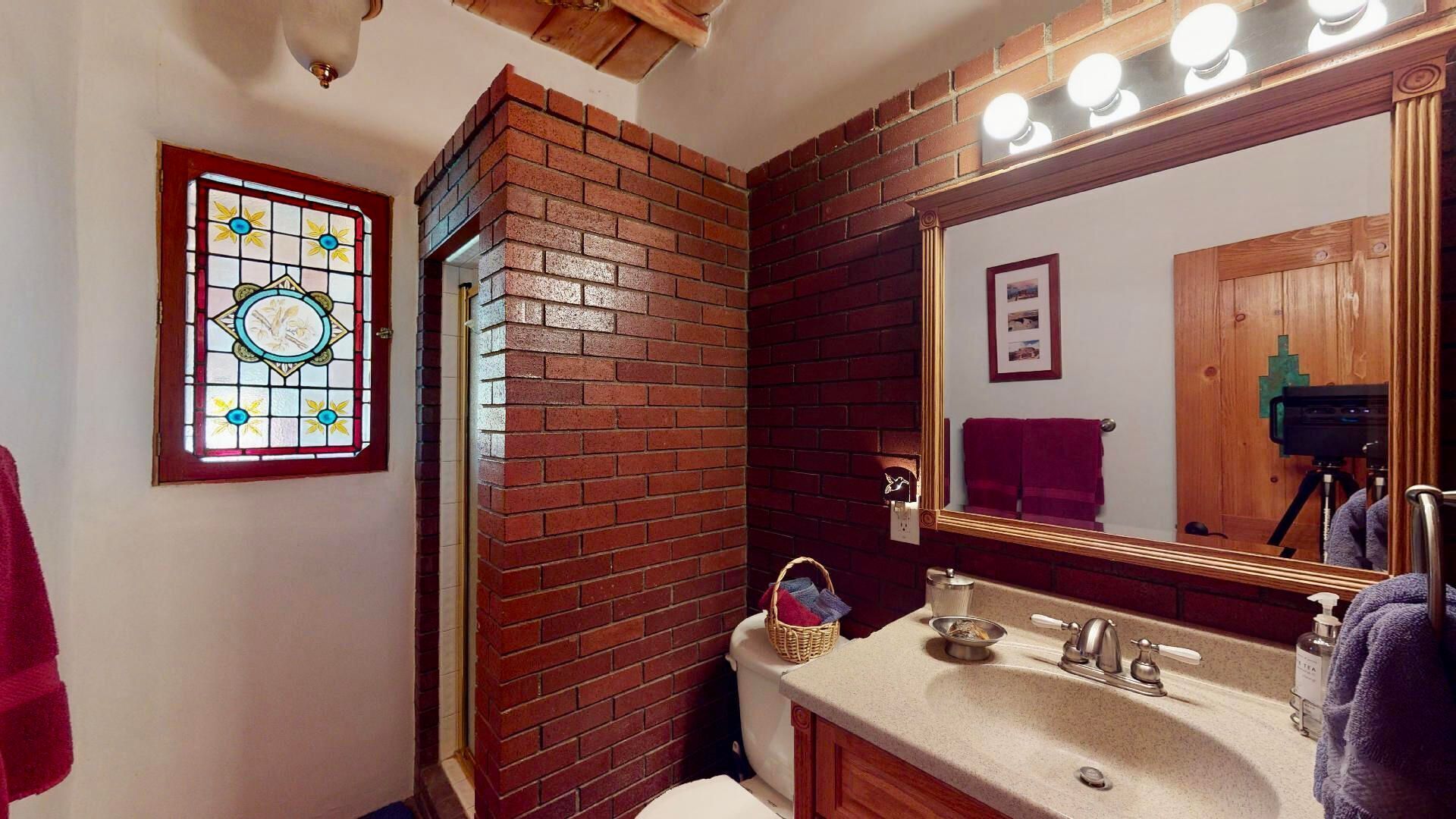 Une salle de bain avec un mur en briques, un vitrail, un lavabo avec un miroir et un porte-serviettes.
