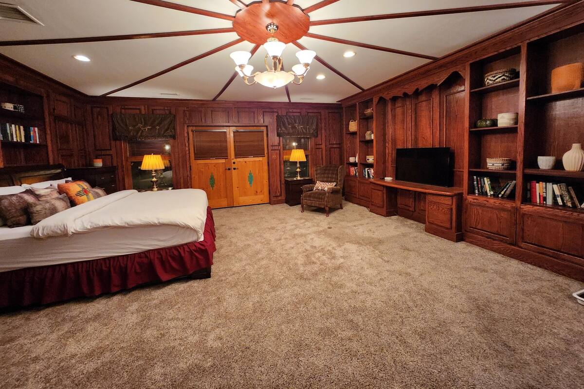 Un dormitorio amplio con una cama grande, televisor, estanterías de madera y un ventilador de techo.