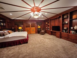 Um quarto espaçoso com uma cama grande, televisão, estantes de madeira e um ventilador de teto.