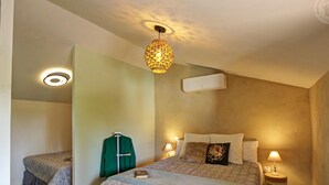 Un dormitorio con una cama grande, dos mesitas de noche, una lámpara colgante y un equipo de aire acondicionado en la pared.