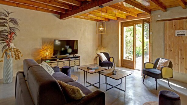 Un salón amplio con techo de madera, un televisor de pantalla plana, asientos cómodos y un ventanal que proporciona luz natural.