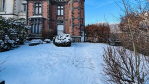 Un grand bâtiment historique à la façade symétrique, doté d’une tour imposante et d’un jardin recouvert de neige.