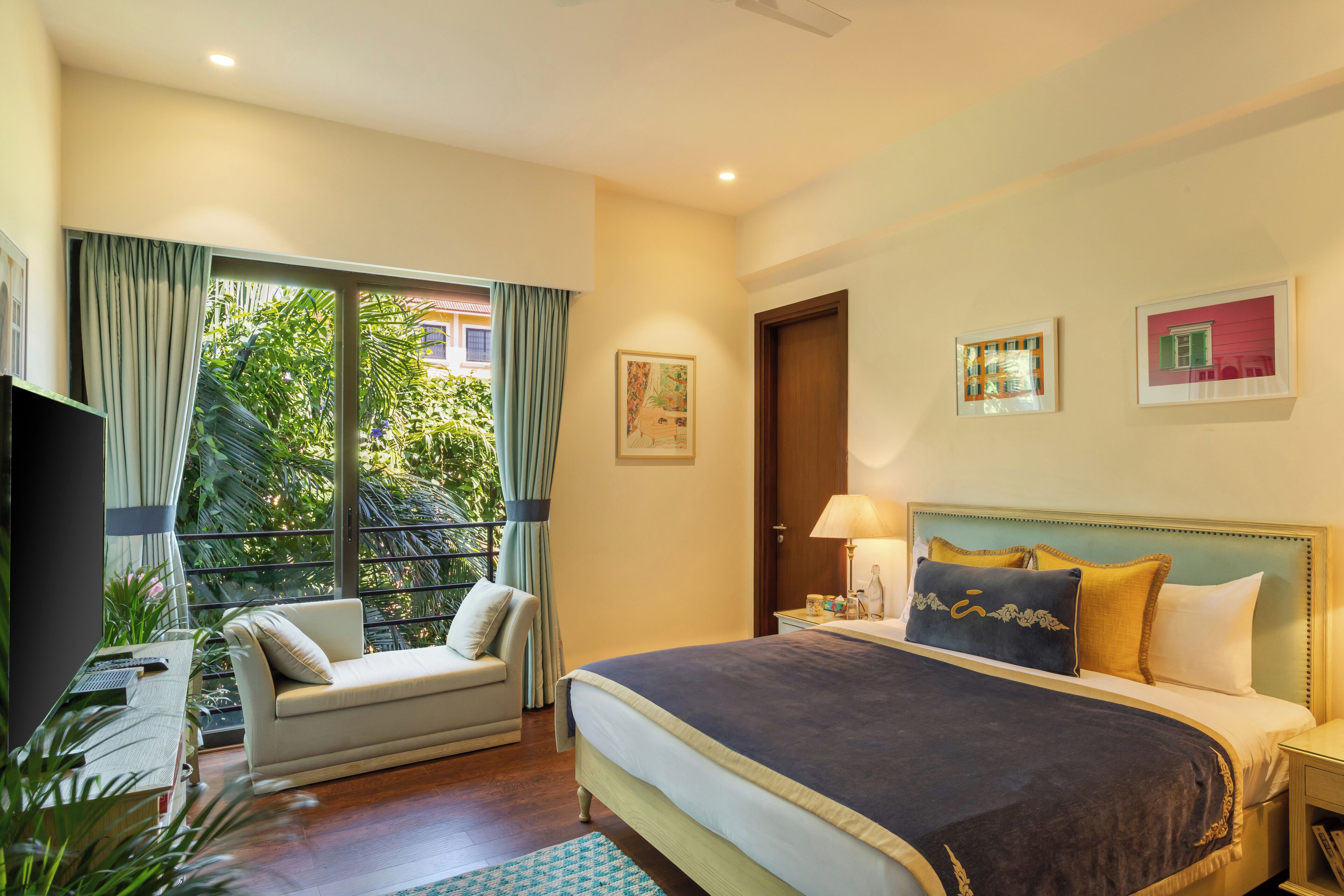 Ein Hotelzimmer mit einem großen Bett, einer Couch, einem Schreibtisch mit Computer und einem Fenster mit Vorhängen.