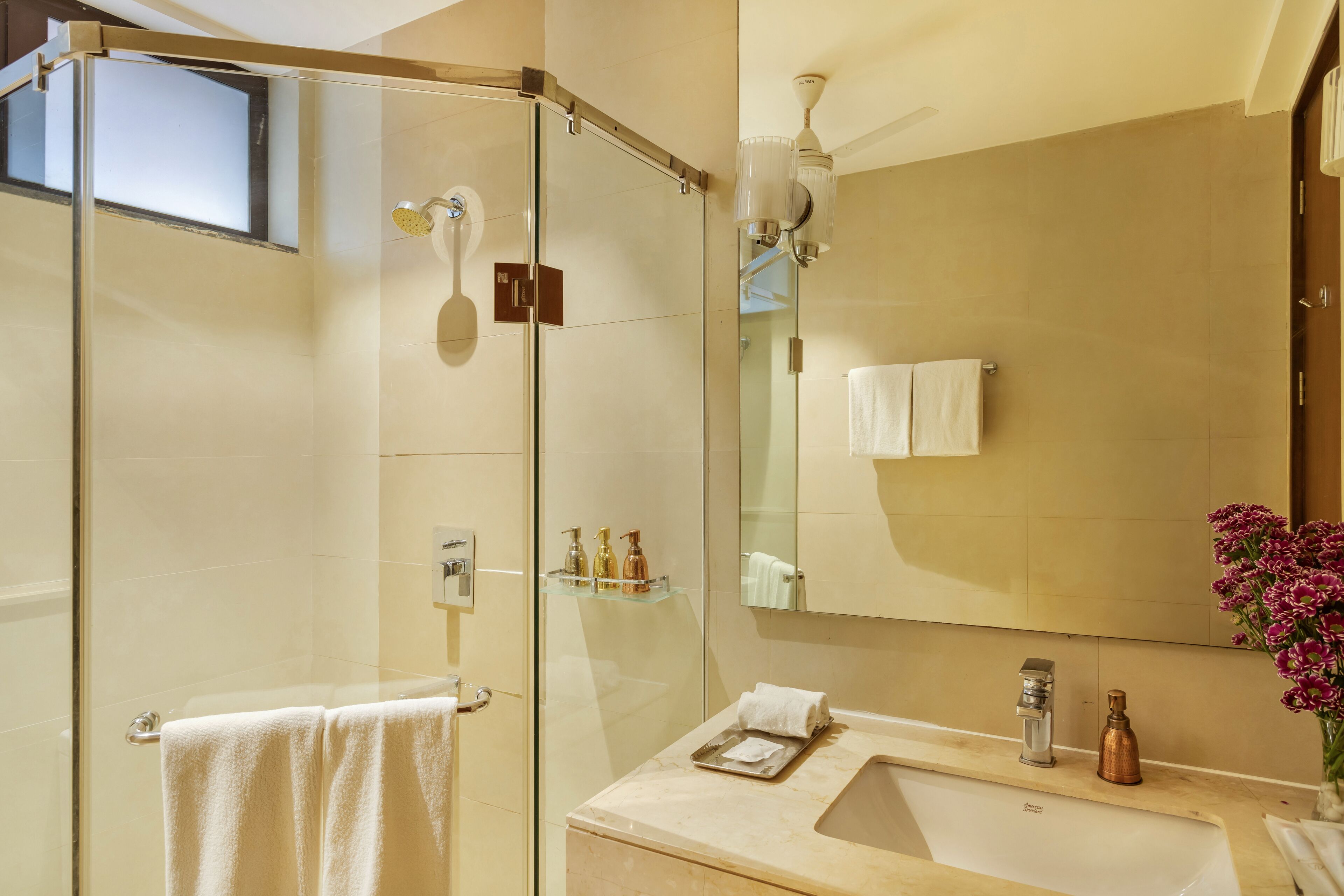 A modern bathroom with a glass-enclosed shower, a sink with a mirror, and a vase of flowers.
