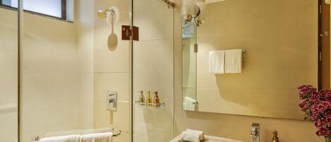 A modern bathroom with a glass-enclosed shower, a sink with a mirror, and a vase of flowers.