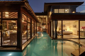 A modern hotel with a swimming pool, large glass windows, and a well-lit interior. - Aalia Villas Anjuna, Goa by Aalia Collection (Anjuna)