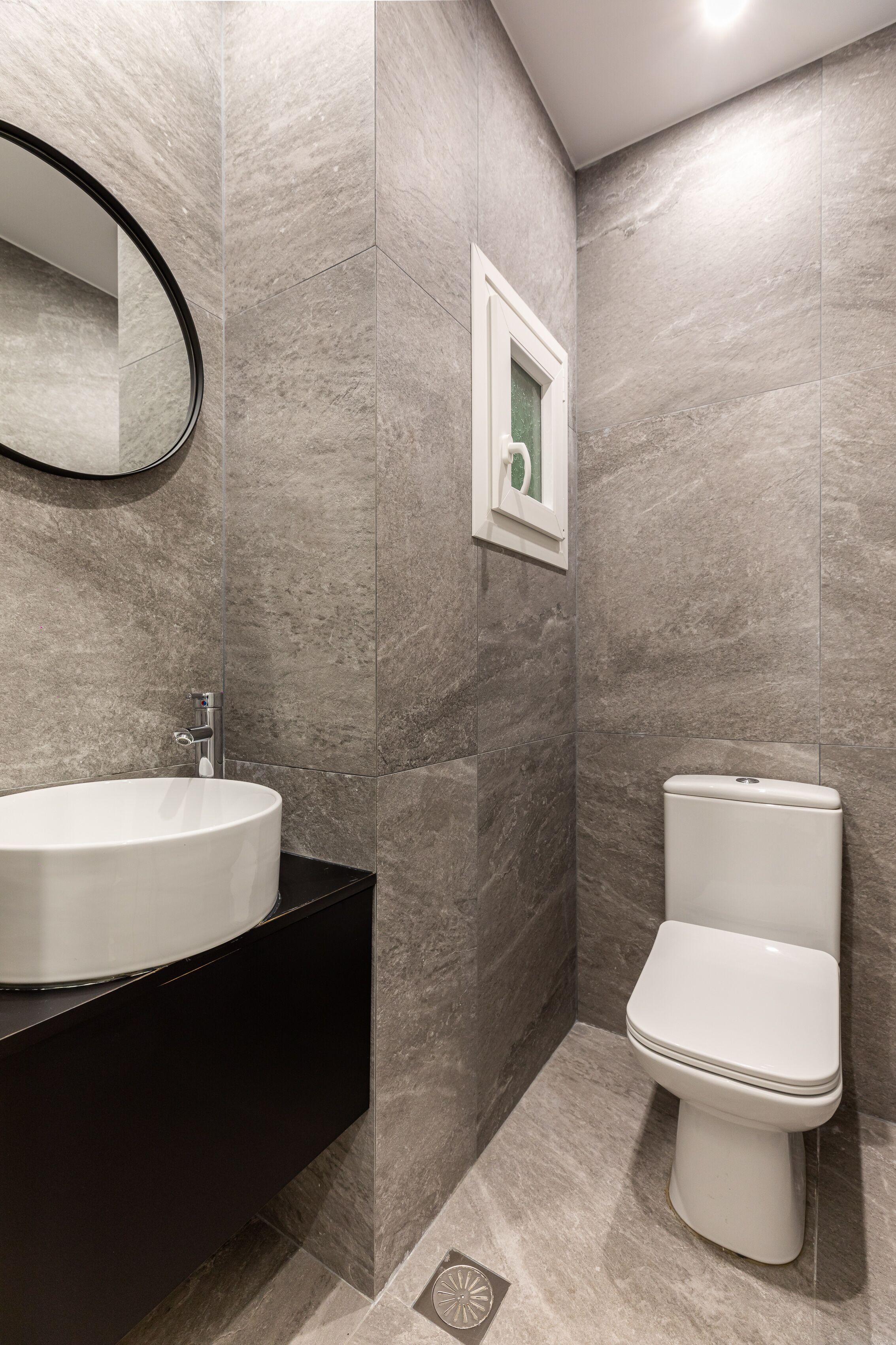 A modern bathroom with a round sink, a toilet, and a mirror on the wall.