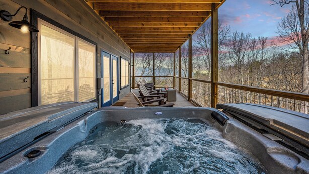 A hot tub area with wooden beams, a view of trees, and a covered deck with seating.
