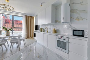 Una cocina moderna con armarios blancos, salpicadero de mármol y vistas a un edificio rojo a través de amplias ventanas.