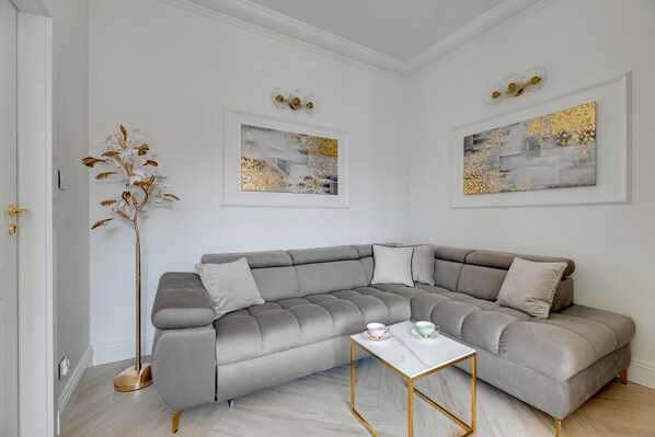 Un salon moderne avec un canapé d’angle gris, une table basse blanche et deux tableaux abstraits aux feuilles d’or qui ornent les murs.