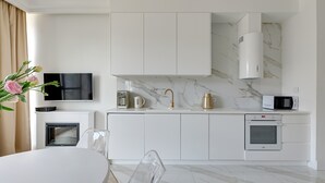 Una cocina moderna con armarios blancos, horno empotrado, microondas y televisor.