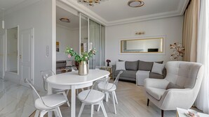 Un salón moderno con una mesa redonda para comer, sillas blancas, un sofá gris y un espejo grande en la pared.