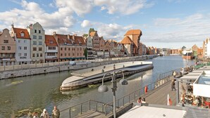 Un paseo junto al río con edificios históricos, un puente y un muelle para embarcaciones.