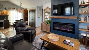 Un salon moderne avec une cheminée, un canapé en cuir et un téléviseur fixé sur un mur bleu.