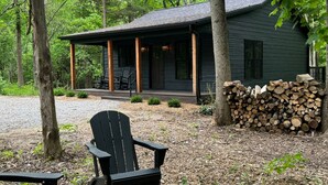 Une cabane avec une véranda, une chaise et une pile de bois de chauffage.