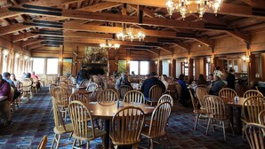 Un vaste espace de restauration intérieur, agrémenté de poutres en bois et de lustres, et comprenant de nombreuses tables et chaises en bois.