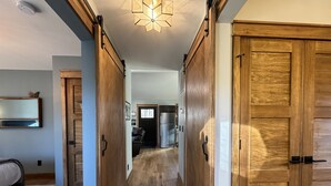Un couloir avec des portes en bois, un lit, un miroir et un luminaire au plafond.