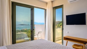 A hotel room with a bed, a TV, a wooden side table, and a balcony with a chair. - Roots Suites in Crete (Agios Nikolaos)