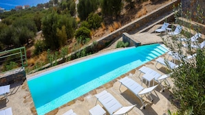 A swimming pool with lounge chairs, surrounded by greenery and overlooking a coastal area. - Roots Suites in Crete (Agios Nikolaos)