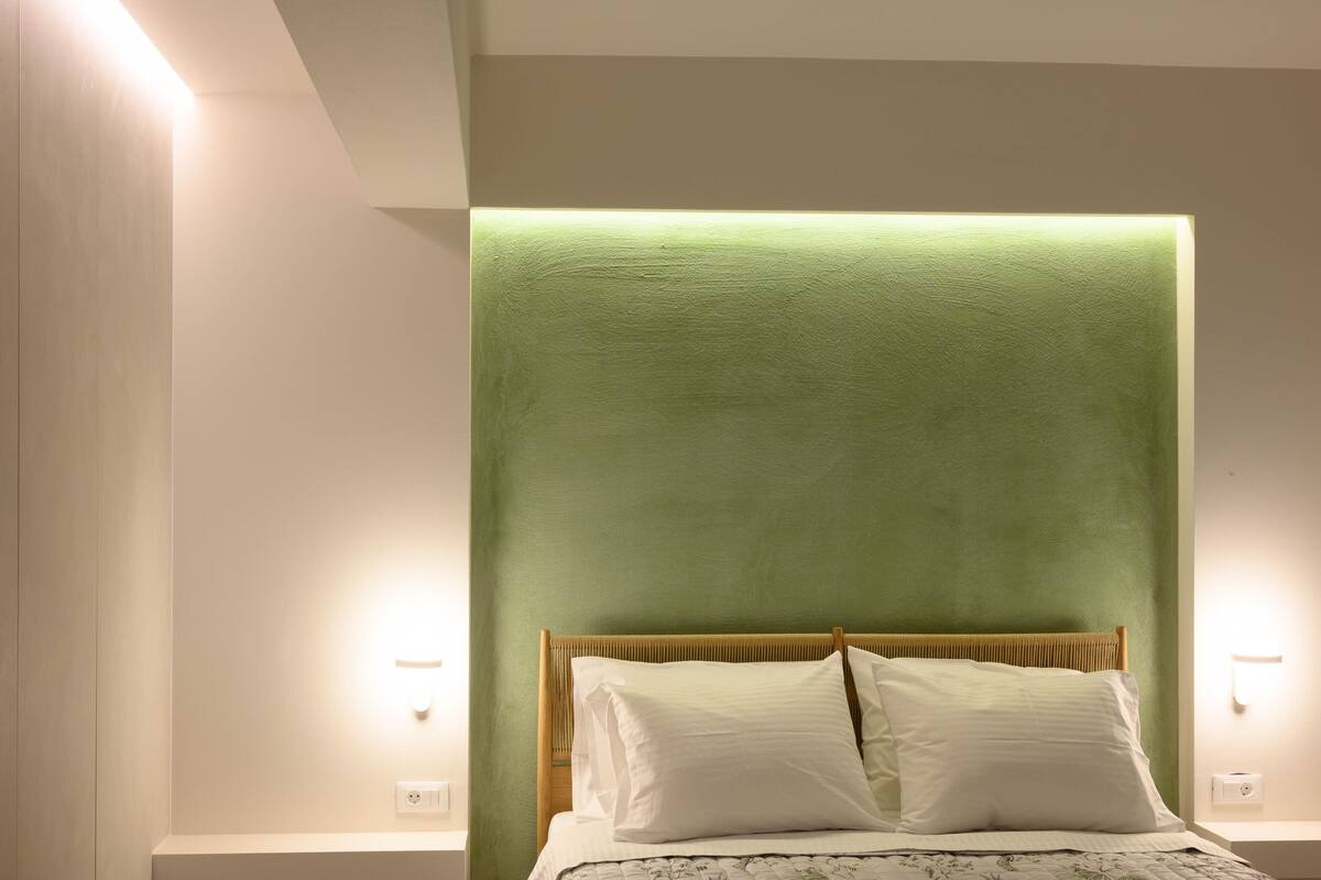 A neatly made bed with white linens and a wooden headboard in a room with green walls and two bedside lamps.