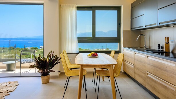 A modern kitchen with a large window, a dining table with chairs, and a view of the sea. - Roots Suites in Crete (Agios Nikolaos)