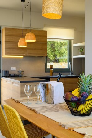 A modern kitchen with wooden cabinets, a dining table with chairs, and a fruit basket.