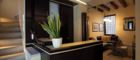 A modern interior with a reception desk, staircase, seating area, and a large window with a geometric pattern.