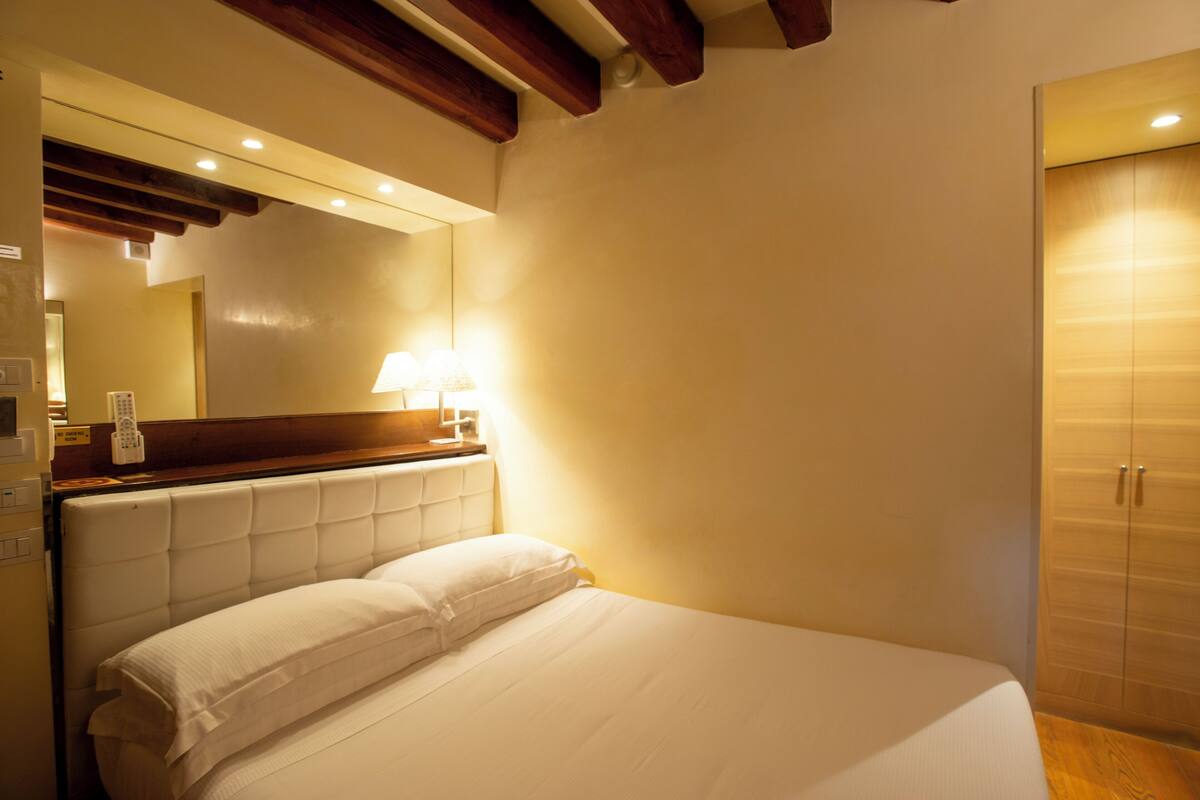 A hotel room with a large bed, a wooden headboard, a bedside table with a lamp, and a wardrobe.