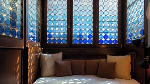 Una cama con cabecera, almohadas y una ventana con paneles de vidrio azul.