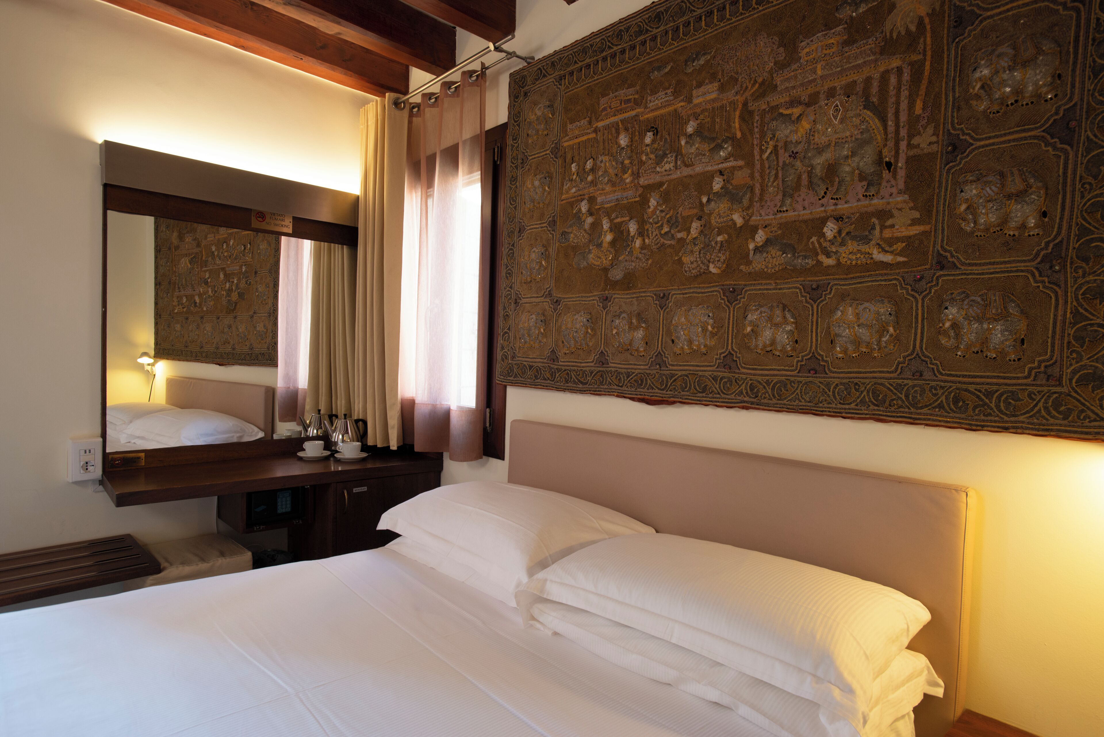 Habitació d'hotel amb un llit, una tauleta de nit, un mirall i un panell decoratiu a la paret.