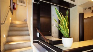 Una escalera con barandilla, una planta en maceta y un extintor en la pared.
