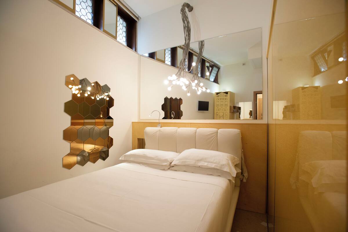 A bedroom with a bed, a wall-mounted hexagonal light fixture, and a wooden headboard.