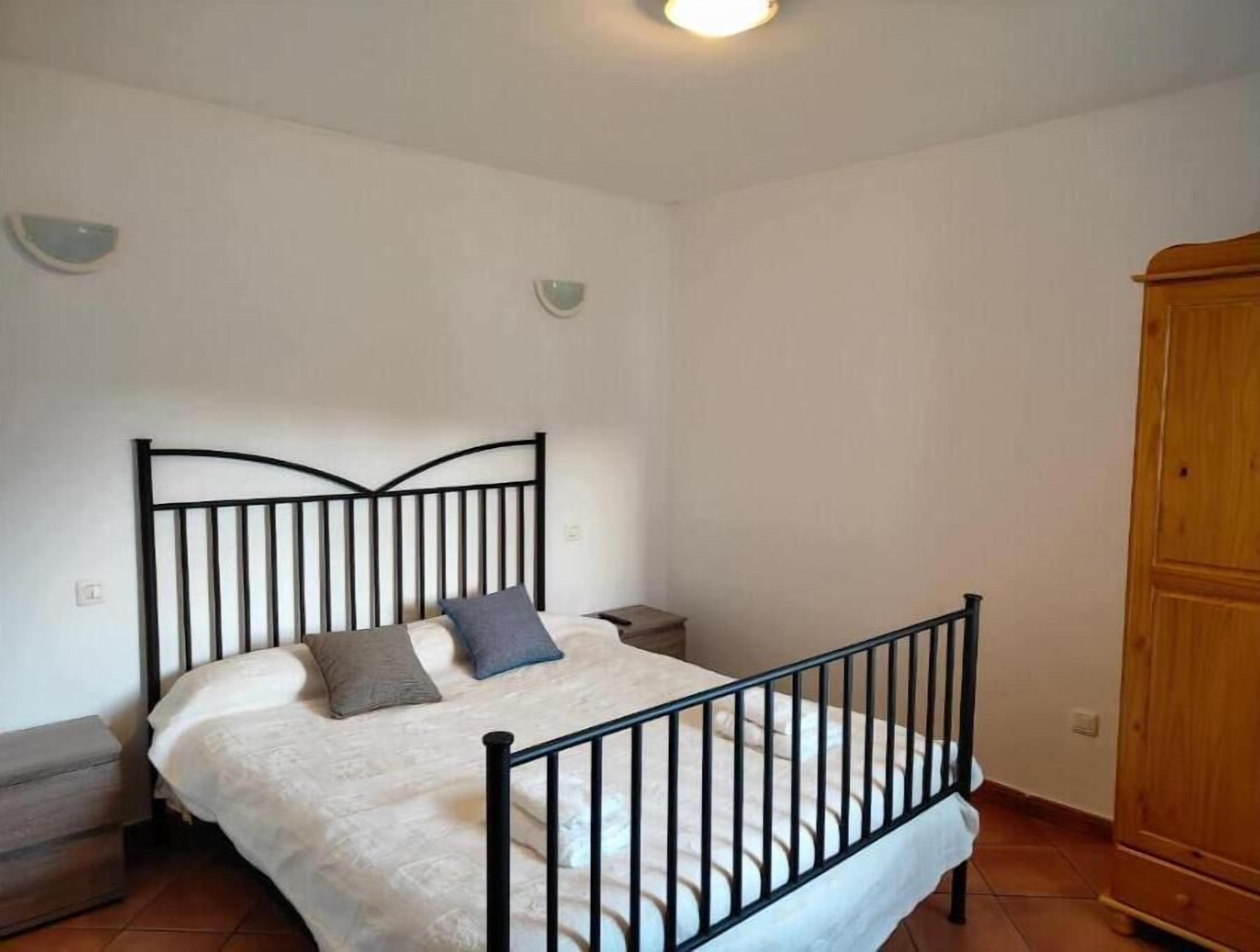 A bedroom with a bed, a wooden wardrobe, and a small bedside table.