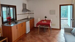 A compact kitchen with a dining area, a window with blinds, and a door leading outside.