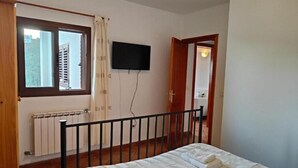 A bedroom with a bed, a window, a radiator, and a television on the wall.