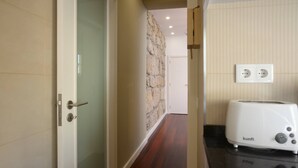 A hallway with a stone accent wall, a door with a glass panel, and a kitchen area with a white toaster on the counter. - Oporto Yellow Villas 7 (Porto)