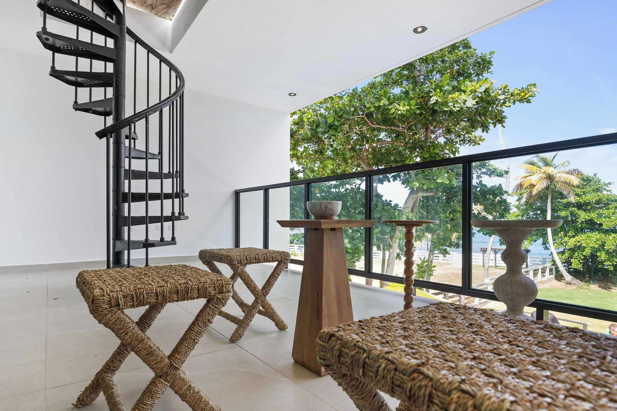 Un interior moderno con una escalera de caracol, muebles de mimbre y vistas a zonas verdes.
