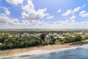 A coastal residential area with beachfront properties, dense vegetation, and a clear sky.