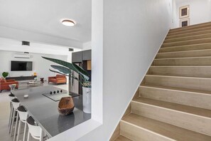 A modern kitchen with a central island, a staircase, and a living area with a sofa and TV.