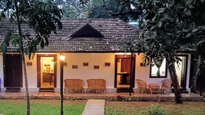 A traditional building with a tiled roof, a porch with chairs, and a well-maintained lawn. - Shantitheeram Ayurveda (Cherthala)