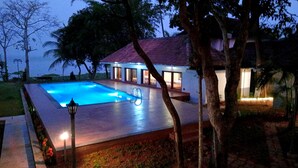 A swimming pool with a red-tiled deck, surrounded by trees and a building with large windows. - Shantitheeram Ayurveda (Cherthala)