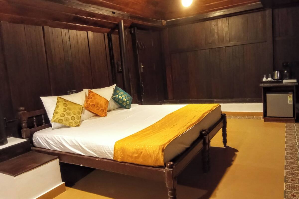 A wooden bed with a white mattress and a yellow blanket, accompanied by patterned pillows.