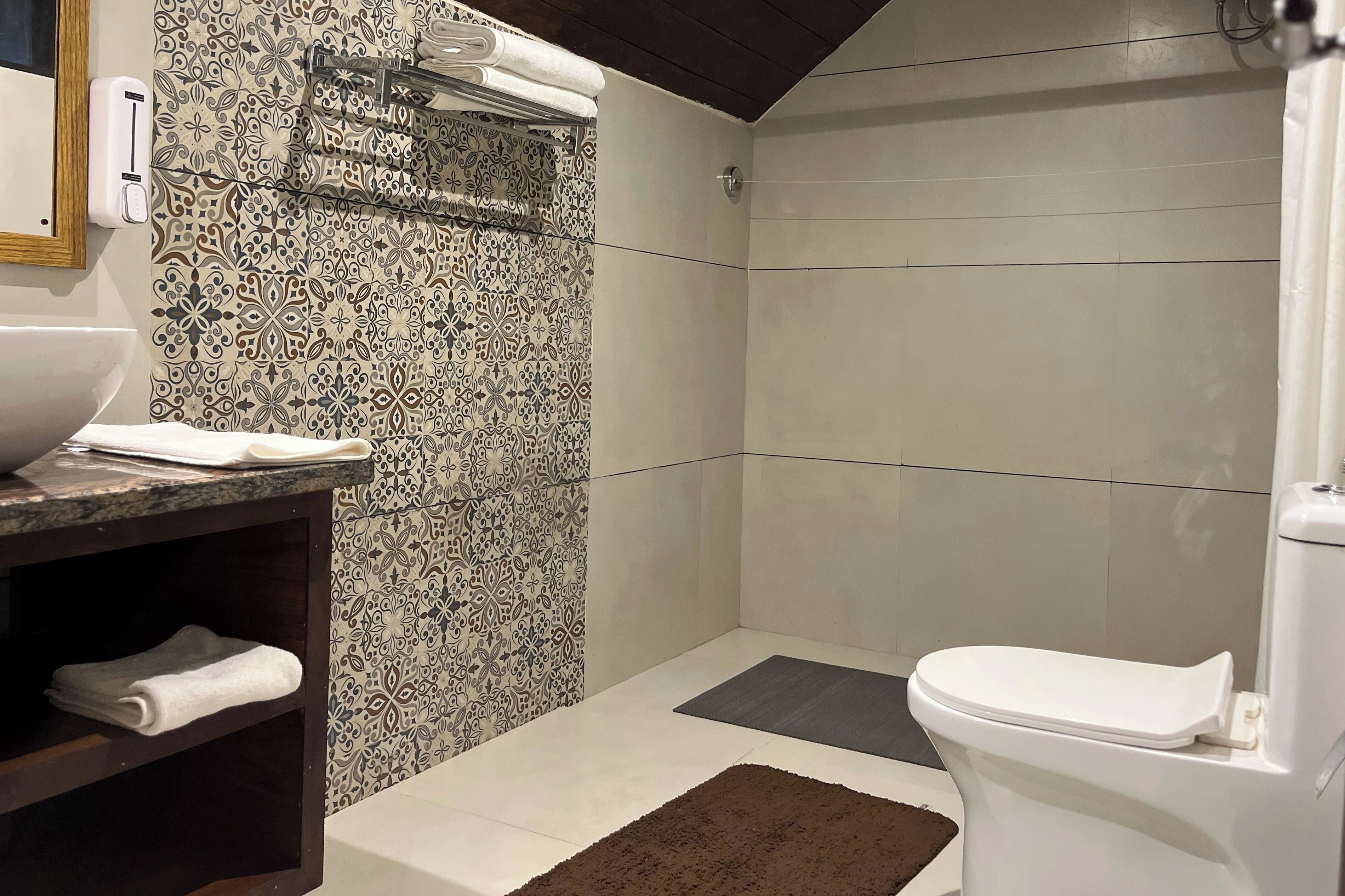 Ein Badezimmer mit einer duschwand mit Muster, einer weißen Toilette, einem Waschbecken mit Marmorplatte und einem Regal mit Handtüchern.