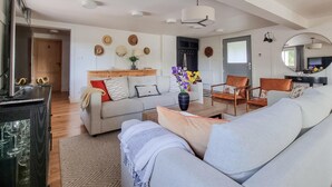 Un salón amplio con sofá, sillones y una mesa de centro. Hay una chimenea, un televisor y un espejo en la pared.
