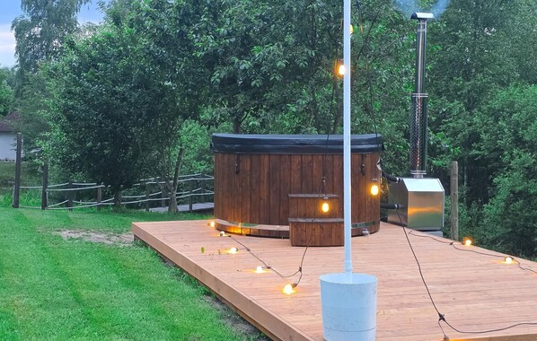 Una terraza de madera con jacuzzi, luces colgantes y un poste alto con una lámpara.